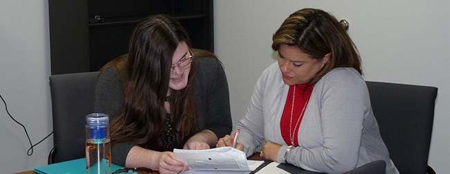 Two woman work together on a packet of papers.