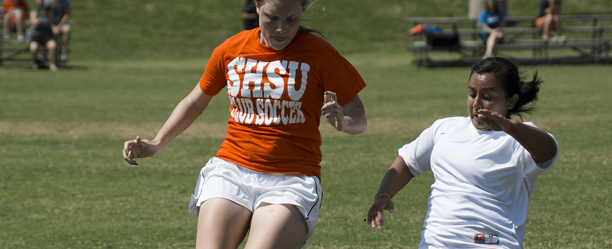 two womens soccer players going after ball on field