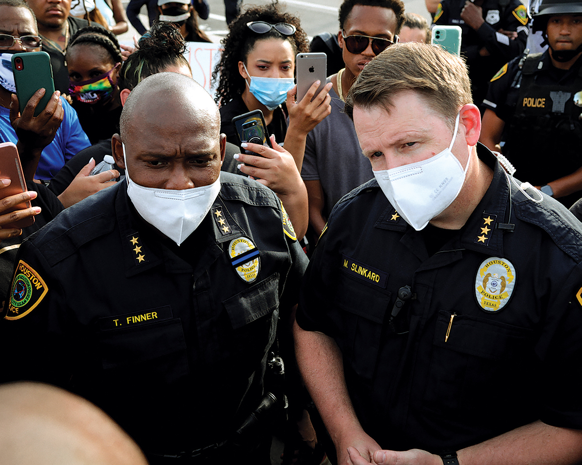 Troy Finner and another officer stand in a crowd that are holding up their cell phones at them.