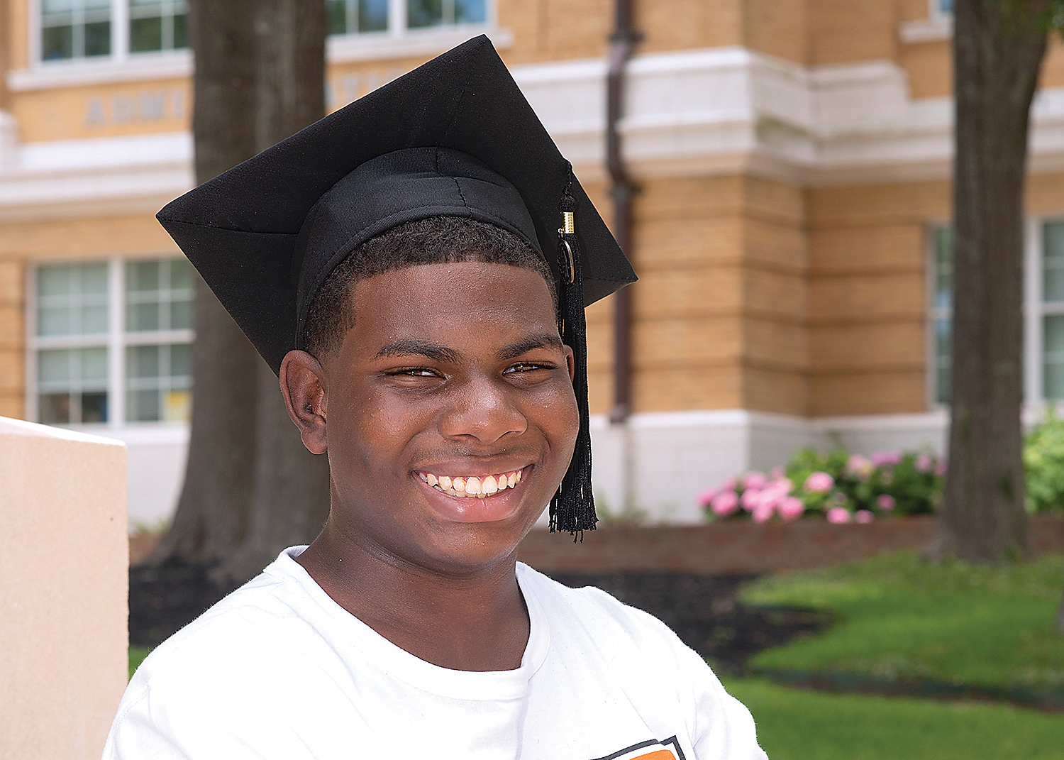 Nehemiah Juniel wears a graduation cap in front of the Administration Building on the Sam Houston State University campus. He smiles proudly.